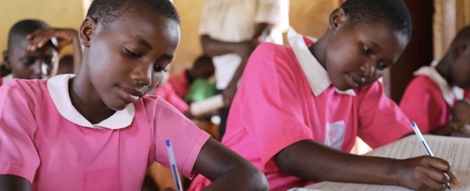 Two girls in pink school uniform do their work at a school in Uganda